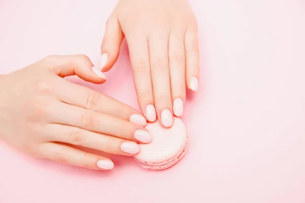 Elegante manicure feminina na moda em fundo rosa. Menina segura as mãos biscoitos de macaron. Vista superior, flat lay — Fotografia de Stock