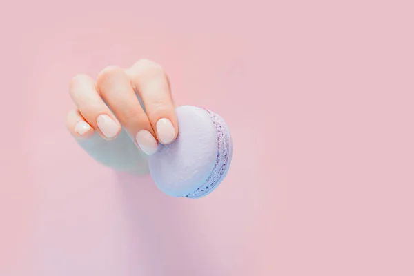 Elegante manicura femenina de moda sobre fondo rosa. Chica sostiene las manos macaron galletas a través del agujero — Foto de Stock