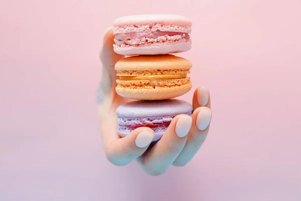 Bonitas mãos menina com unhas manicure moda segurando cor macaroon bolo através de buraco no fundo rosa — Fotografia de Stock