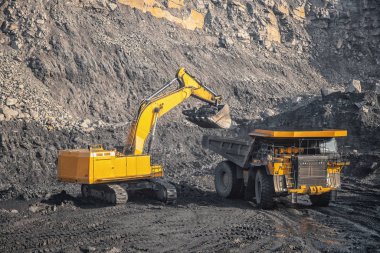 Hydraulic excavator loads coal into body of large yellow mining truck. Open pit mine industry for anthracite