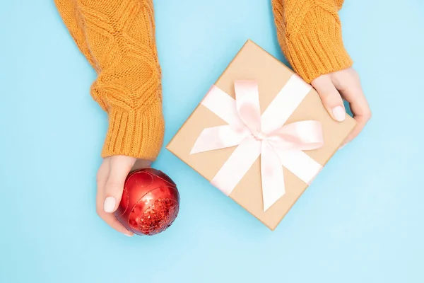 Hermosas manos niña sostienen caja de regalo presente papel artesanal con lazo rosa sobre fondo azul, vista superior. Concepto Navidad, Año Nuevo — Foto de Stock