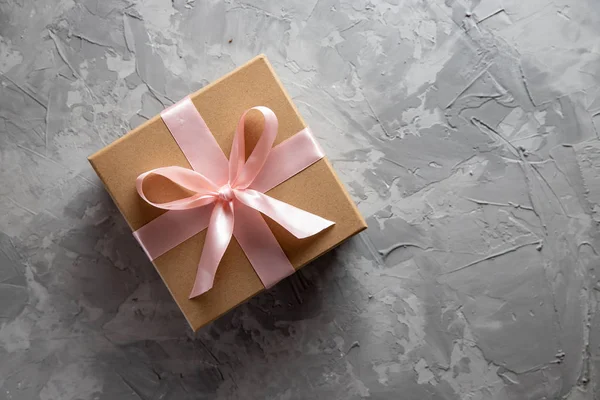 Caja de regalo con arco de cartón kraft sobre fondo gris, vista superior. Concepto sorpresa, regalo de cumpleaños — Foto de Stock