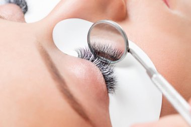 Kirpik uzatma prosedürü. Cımbız ustası güzel bir kadına sahte kirpik takar.