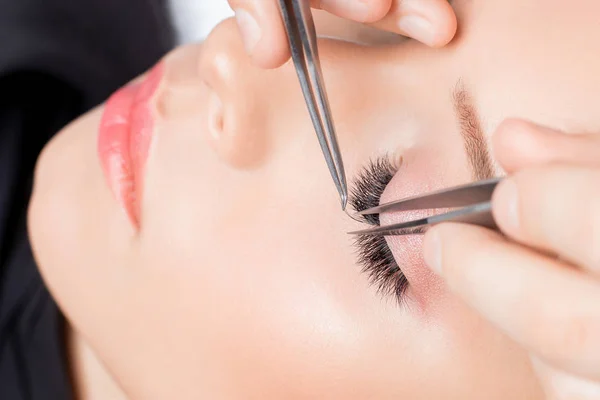 Eyelash extension procedure. Master tweezers fake long lashes beautiful female eyes