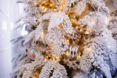 Noel ağacı arka planında yapay karla süslenmiş oyuncak topları, dallı altın aydınlatma