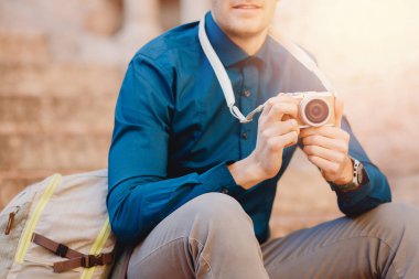Elinde küçük kamera, mavi gömlek ve sırt çantası olan gezgin bir erkek fotoğrafçı.