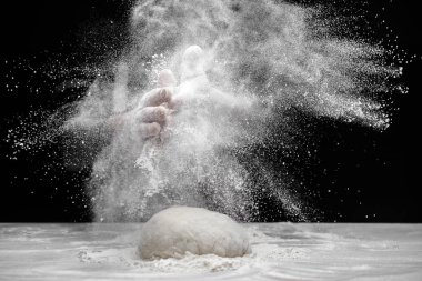 Beyaz un, siyah arka planda havada uçuşuyor. Pasta şefi el çırpıyor ve pizza hamuru hazırlıyor.