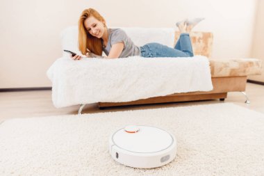 Genç kız halı üzerinde çalışan otomatik akıllı robot süpürge kullanıyor.