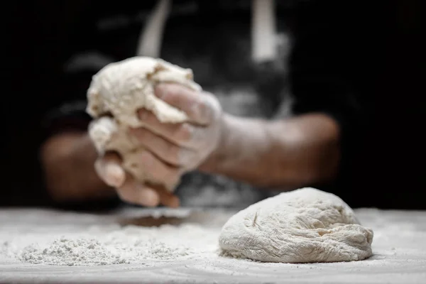 Mains de boulanger masculin préparant la pâte à levure avec de la poussière de farine blanche sur fond noir, ramasser pour les pâtes et la pizza — Photo