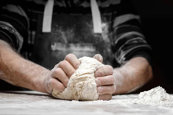 La farine blanche vole dans l'air sur fond noir, le pâtissier applaudit les mains et prépare la pâte à levure pour les pâtes à pizza — Photo