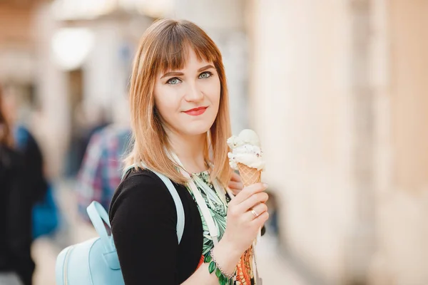 Красивая девушка турист держит и ест итальянское мороженое в конусе и смотрит в рамку, синий рюкзак — стоковое фото