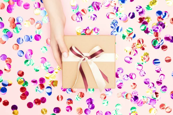 Hermosas manos chica celebrar regalo regalo caja regalo presente papel artesanal sobre fondo de confeti rosa. Concepto Navidad, Año Nuevo — Foto de Stock
