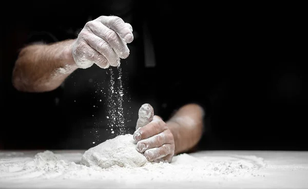 Harina blanca vuela en el aire sobre fondo negro, pastelero aplaude las manos y prepara la masa de levadura para la pasta de pizza — Foto de Stock