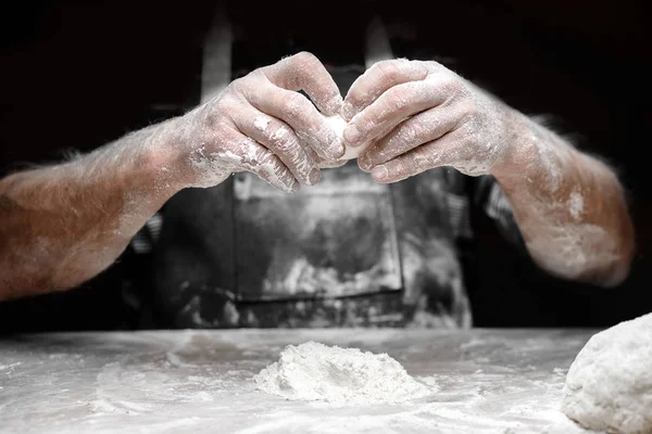 Baker szakács szórás liszt friss tészta a konyhaasztalon, fekete háttér — Stock Fotó