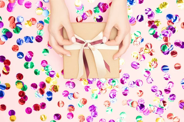 Hermosas manos femeninas corbata lazo festivo en la caja de regalo presente en el fondo de confeti rosa. Concepto Navidad, Año Nuevo — Foto de Stock