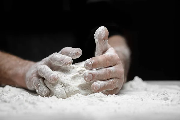 Mains de boulanger masculin préparant la pâte à levure avec de la poussière de farine blanche sur fond noir, ramasser pour les pâtes et la pizza — Photo