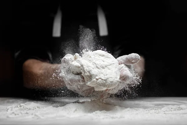 Mãos padeiro preparando massa de levedura com farinha de poeira branca no fundo preto, colher para massas e pizza — Fotografia de Stock