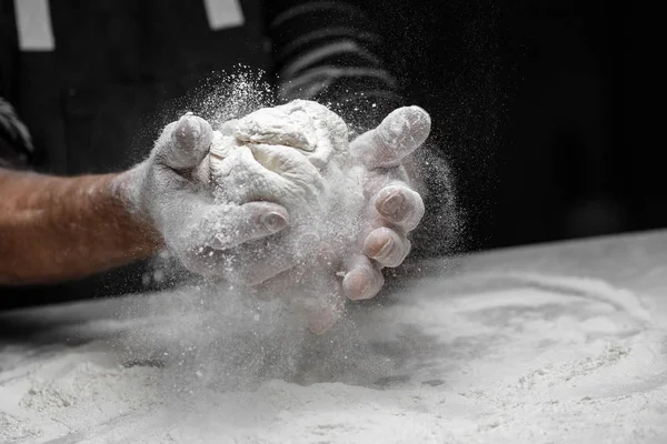 Mãos padeiro preparando massa de levedura com farinha de poeira branca no fundo preto, colher para massas e pizza — Fotografia de Stock