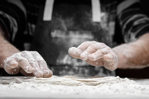 Mains de boulanger masculin préparant la pâte à levure avec de la poussière de farine blanche sur fond noir, ramasser pour les pâtes et la pizza — Photo