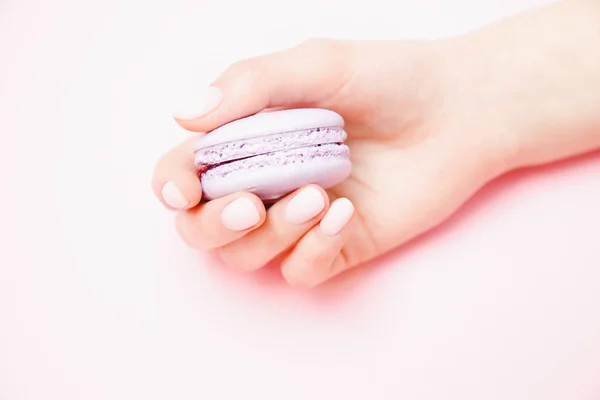 Elegante manicura femenina de moda sobre fondo rosa. Chica toma de las manos galletas macaron violeta. Concepto cuidado de la piel —  Fotos de Stock