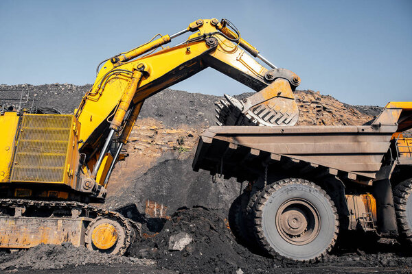 Open pit mine industry, excavator loading coal on big yellow mining truck for anthracite