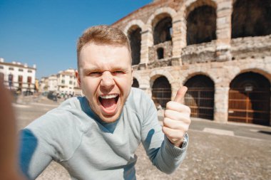 Mutlu erkek gezgin, İtalya 'nın Verona şehrindeki amfitiyatro kolezyumunun arka planında selfie çekiyor. Seyahat kavramı