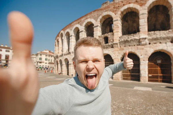 Щасливий чоловік - мандрівник робить самовіддану фотографію на задньому плані амфітеатру в місті Вероні, Італія. Концепція подорожі — стокове фото