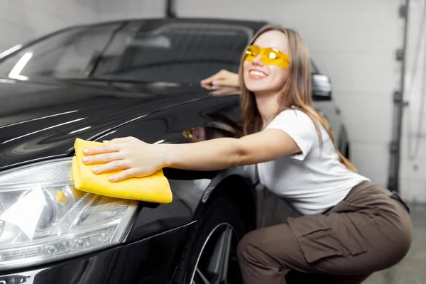 Hand worker girl lucida e pulisce i fari in microfibra su auto nera. Concetto servizio di lavaggio auto — Foto Stock