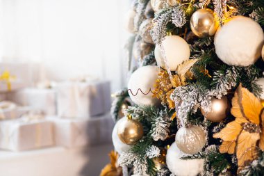 Beyaz toplar ve altın yaylarla süslenmiş Noel ağacı, arka planda gümüş hediyeler