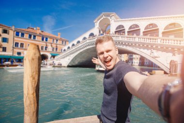 Venedik, İtalya 'da gülümseyen genç bir adam büyük kanal ve köprüye selfie çekiyor. Seyahat kavramı