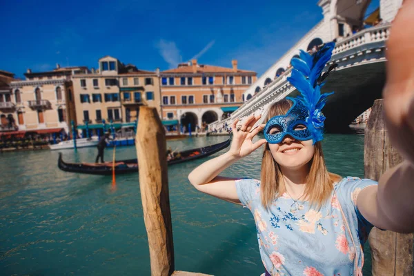 Portrait smiling young woman in Venice, Italy taking selfie while in Venetian blue mask against backdrop of great canal and bridge. Concept travel — 스톡 사진