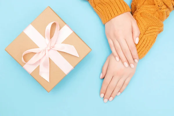 Hermosas manos femeninas con manicura rosa en las uñas en un cálido suéter de punto fondo azul con baht caja artesanal de regalo. Concepto regalo San Valentín, Cumpleaños, Navidad — Foto de Stock