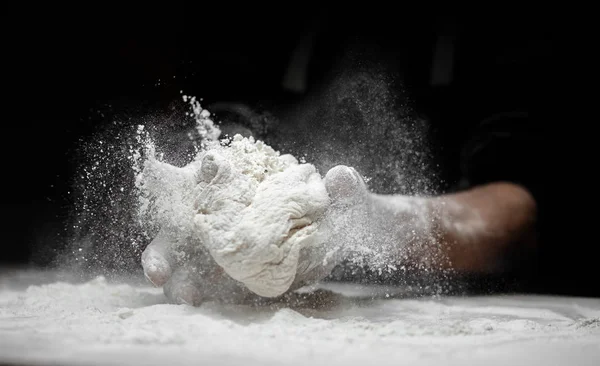 Dłonie piekarza przygotowującego ciasto drożdżowe z białym pyłem mąki na czarnym tle, szufelka na makaron i pizzę — Zdjęcie stockowe