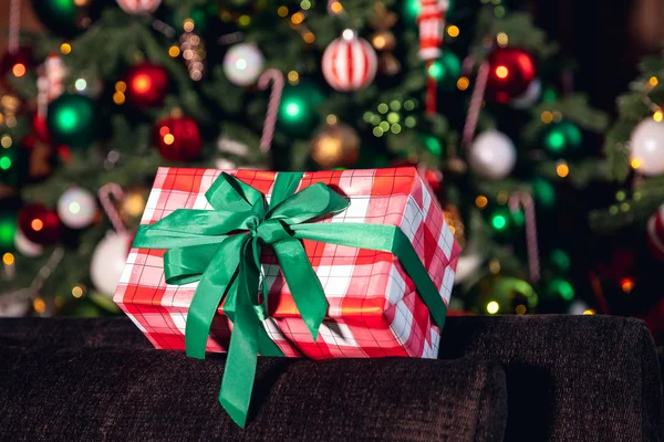 Νέο Έτος δώρο με κόκκινο πλέγμα γραμμές, δεμένα πράσινη κορδέλα στο φόντο του χριστουγεννιάτικου δέντρου με φωτισμό — Φωτογραφία Αρχείου