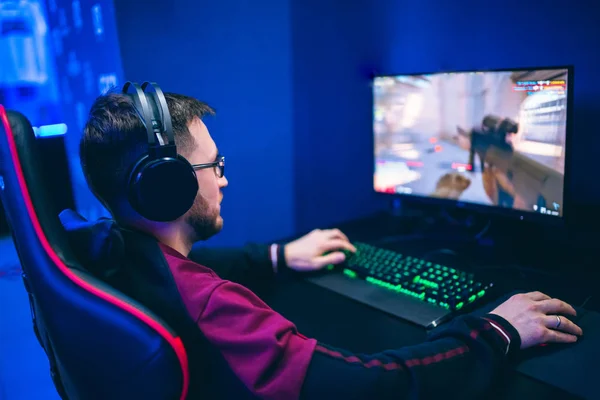 Jugador profesional jugando torneos de juegos en línea ordenador PC con auriculares, fondo rojo y azul borrosa —  Fotos de Stock