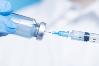 Doktorun elinde mavi eldivenli beyaz önlüklü şırınga ve aşı var. Enjeksiyon konsepti