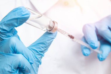 Doktor elinde şırınga ve aşıyı mavi eldivenli, beyaz önlüklü, güneş ışığında tutuyor. Hastalık enjeksiyonu