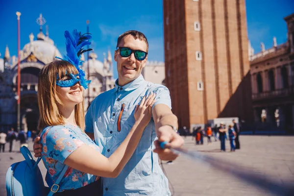 Casal amante selfie tirar fotos viagens Veneza, Itália contra o pano de fundo St Mark Square em máscara veneziana azul — Fotografia de Stock