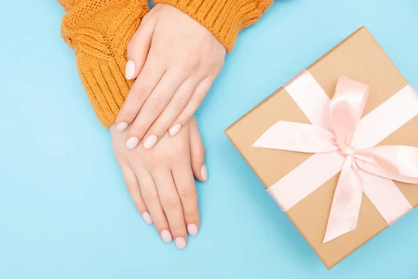 Hermosas manos femeninas con manicura rosa en las uñas en el suéter de punto cálido fondo azul con baht caja de artesanía de regalo, vista superior — Foto de Stock