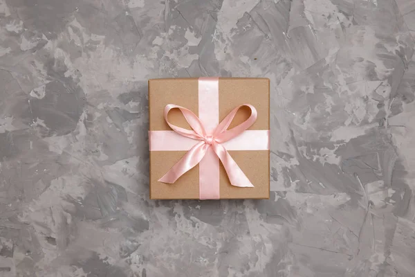 Caja de regalo con arco de cartón kraft sobre fondo gris, vista superior. Concepto sorpresa, regalo de cumpleaños — Foto de Stock