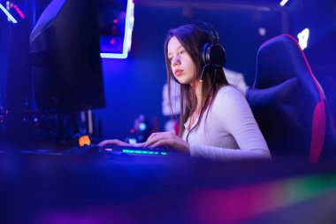 Streamer güzel kız profesyonel oyuncu gülümsemesi çevrimiçi oyunlar oynuyor kulaklıkla bilgisayar, neon rengi