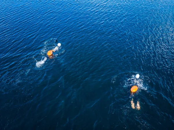 Arctic people swim ice hole in cold water, athletes in wetsuits with orange buoys in blue sea