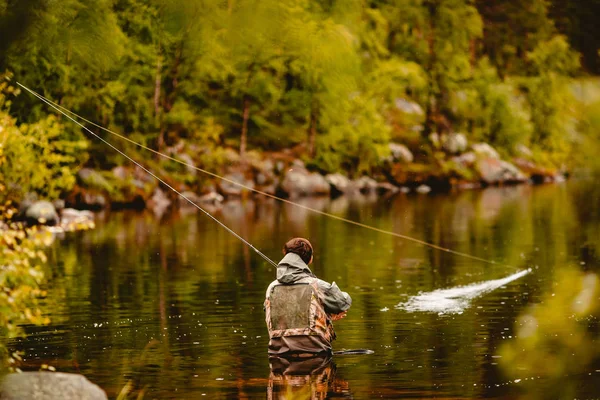 Pescatore con canna pesca a mosca nel fiume mattina in piedi in acqua — Foto Stock