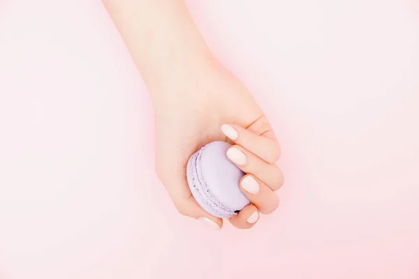 Elegante manicure feminina na moda em fundo rosa. Menina segura as mãos biscoitos de macaron. Vista superior, flat lay — Fotografia de Stock