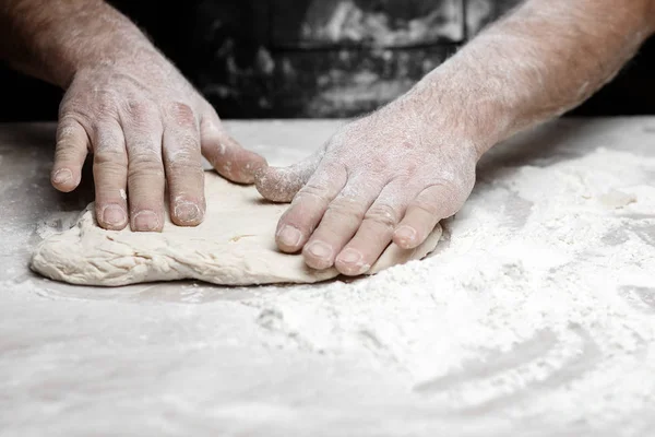 Mains de boulanger masculin préparant la pâte à levure avec de la poussière de farine blanche sur fond noir, ramasser pour les pâtes et la pizza — Photo
