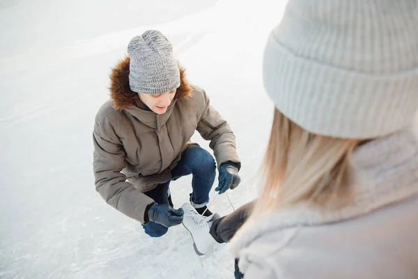 El hombre ayuda a ponerse patines de figura blanca para la pista de patinaje a la hermosa niña en el fondo de la nieve en invierno, el concepto es el cuidado del amor, la relación entre las personas — Foto de Stock