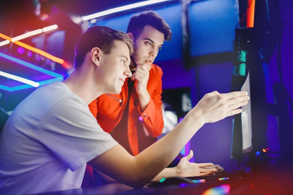 オンラインビデオゲームをプレイする2人の男のチームは、インターネットカフェでコンピュータモニターの後ろで戦う戦略を分析します。 — ストック写真