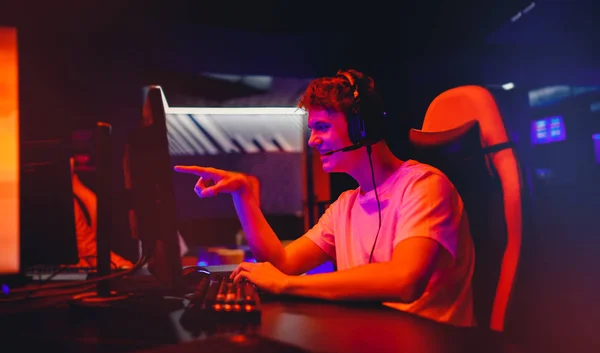 Gamer νεαρός άνδρας παίζει σε απευθείας σύνδεση υπολογιστή βιντεοπαιχνίδια και σημεία για να παρακολουθεί με το δάχτυλο, νέον χρώμα — Φωτογραφία Αρχείου
