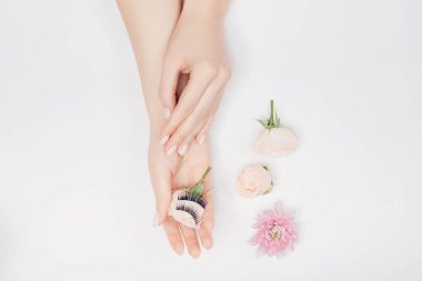 Güzellik modası kavramı. Arka planda beyaz çiçekli el hatunuyla sahte kirpiklerin uzantısı