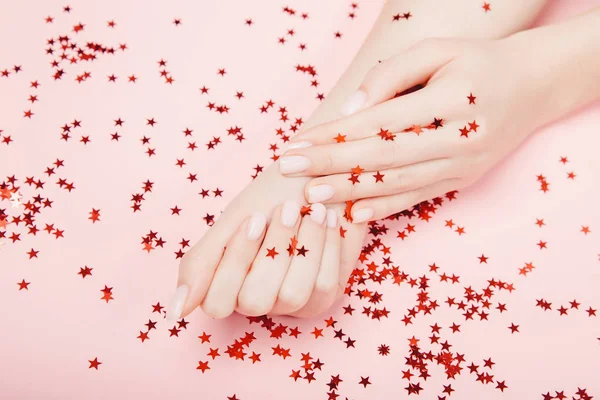 Elégant ongle tendance jeune femme mains manucure rose sur fond avec confettis étoile rouge — Photo